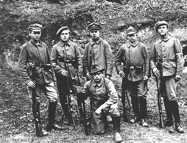 Six Polish soldiers from the Polish Legions, five standing and one kneeling, pose with rifles and wearing uniforms with caps and hats.